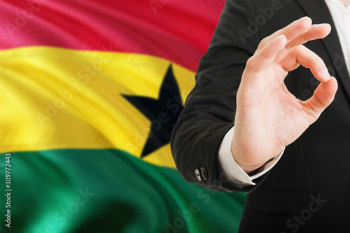Ghana acceptance concept. Elegant businessman is showing ok sign with hand on national flag background. © sezerozger