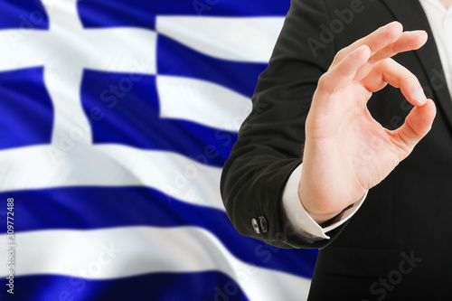 Greece acceptance concept. Elegant businessman is showing ok sign with hand on national flag background.