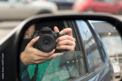 Hidden photographing. Reflection in car mirror of woman with camera. Paparazzi concept