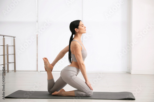Young woman practicing One Legged King Pigeon asana in yoga studio. Eka Pada Rajakapotasana pose
