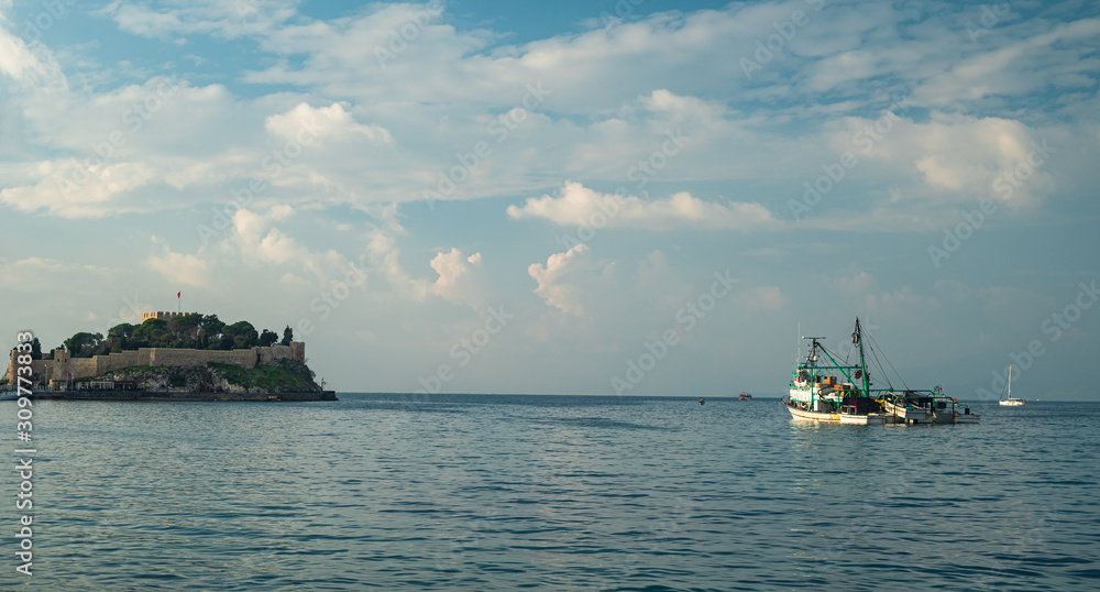 Fishing boat in the sea and the island of Pigeon in the background.  Kuşadası Pigeon Island and dense clouds behind the boat.