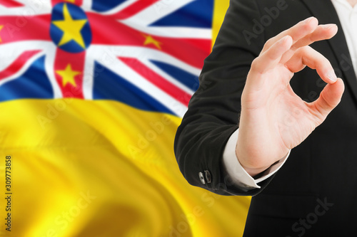 Niue acceptance concept. Elegant businessman is showing ok sign with hand on national flag background.