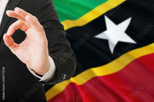 Saint Kitts And Nevis acceptance concept. Elegant businessman is showing ok sign with hand on national flag background.