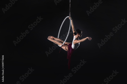 Young woman performing acrobatic element on aerial ring indoors