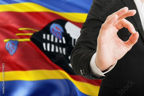Swaziland acceptance concept. Elegant businessman is showing ok sign with hand on national flag background.