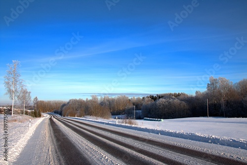 Beautiful sunny winter day with white trees and asphalt road in the foreground