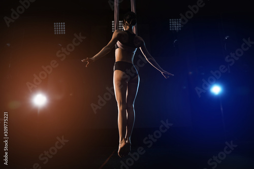 Young woman performing acrobatic element on aerial silk indoors © New Africa