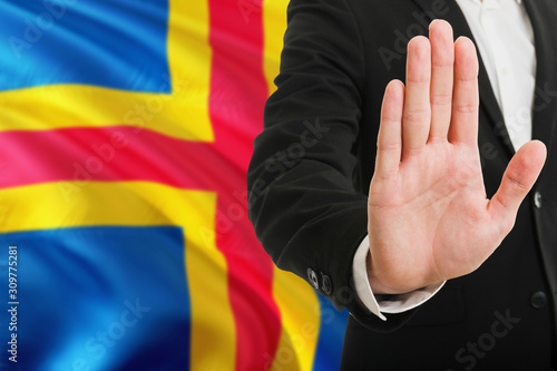 Aland Islands rejection concept. Elegant businessman is showing stop sign with hand on national flag background.