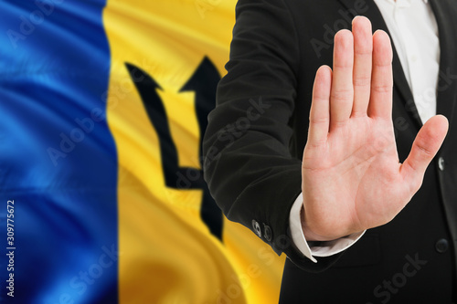Barbados rejection concept. Elegant businessman is showing stop sign with hand on national flag background.