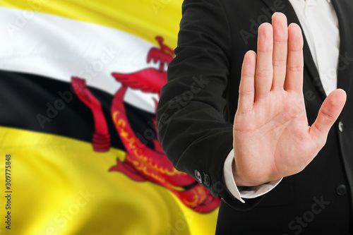 Brunei rejection concept. Elegant businessman is showing stop sign with hand on national flag background.