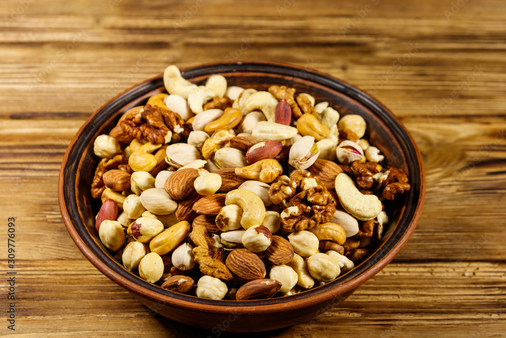 Mixed nuts on wooden table. Walnuts, pistachio, almond, peanut, cashew, hazelnut in ceramic bowl. Healthy eating concept Mixed nuts on wooden table. Walnuts, pistachio, almond, peanut, cashew, hazelnut in ceramic bowl. Healthy eating concept