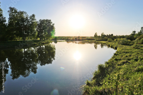 Fototapeta Naklejka Na Ścianę i Meble -  Summer landscape - Calm flat river among fields and birch groves in sunset lighting. Cloudless summer weather.