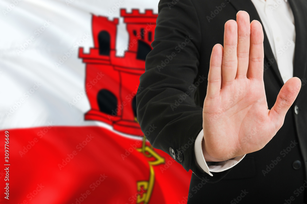 Gibraltar rejection concept. Elegant businessman is showing stop sign with hand on national flag background.