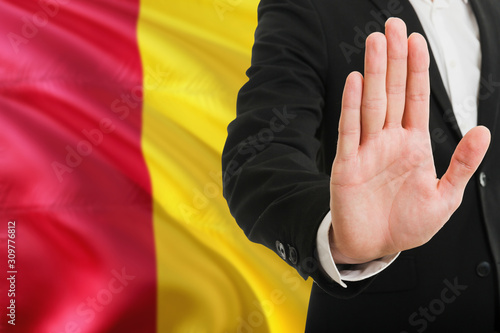 Guinea rejection concept. Elegant businessman is showing stop sign with hand on national flag background.