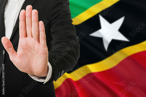 Saint Kitts And Nevis rejection concept. Elegant businessman is showing stop sign with hand on national flag background.