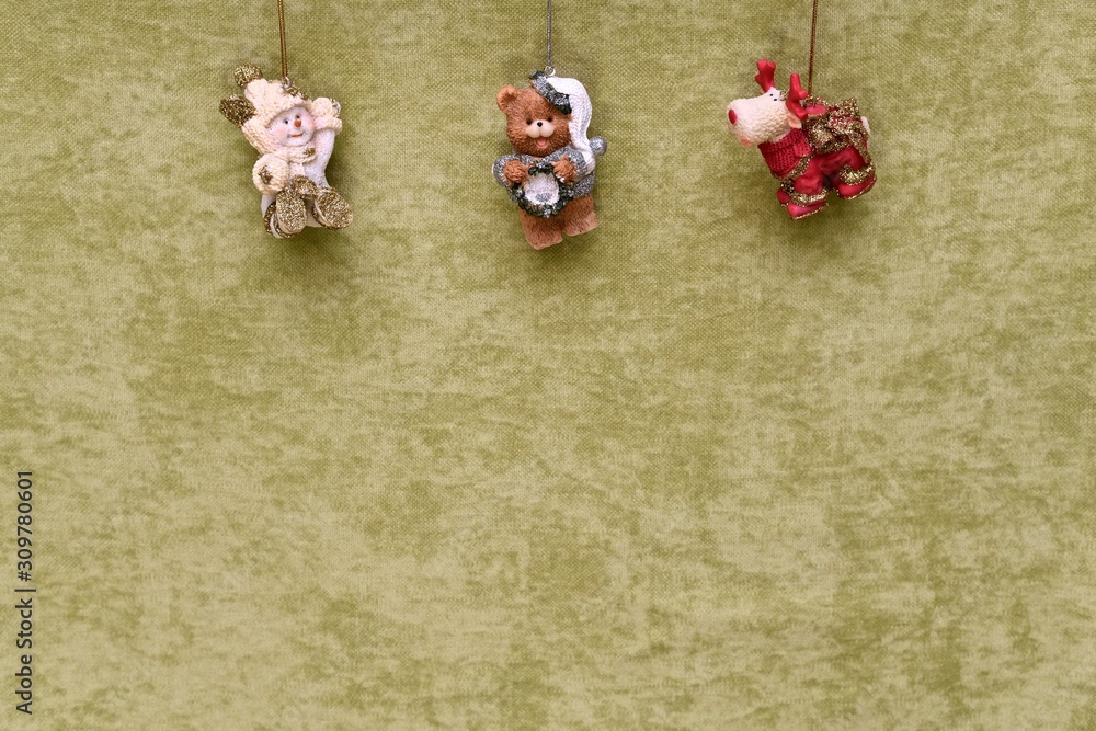 Christmas toys, snowman, teddy bear and deer, suspended at the top, on a green plush background.