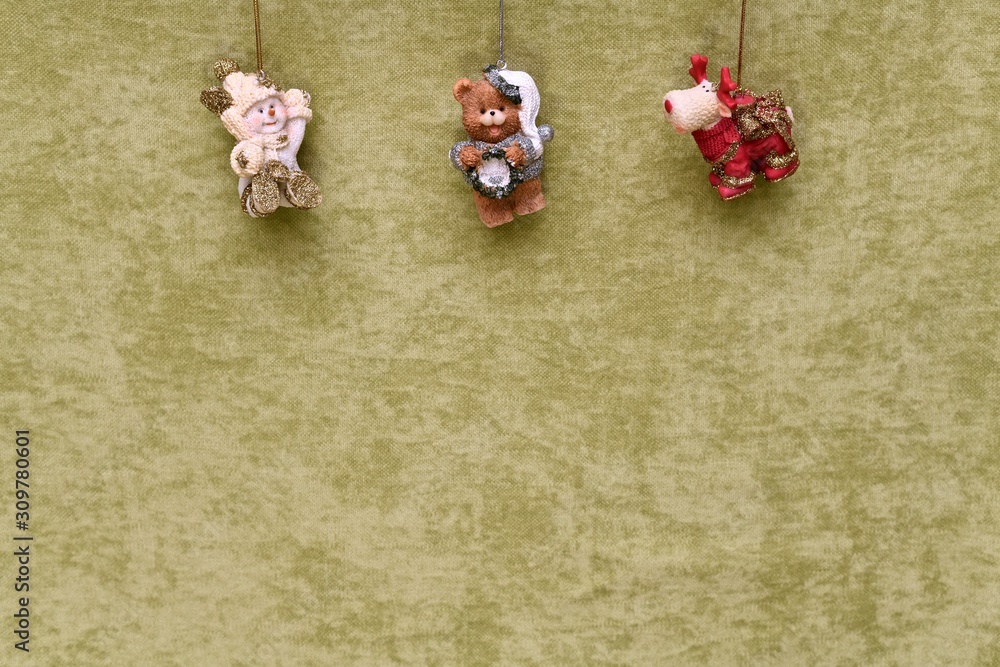 Christmas toys, snowman, teddy bear and deer, suspended at the top, on a green plush background. Christmas toys, snowman, teddy bear and deer, suspended at the top, on a green plush background.