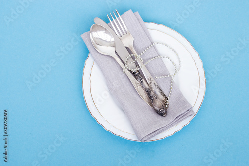 Festive Christmas table setting. Knife, fork, spoon and linen napkin on a blue background. Family holiday concept. Copy space. Flatlay.