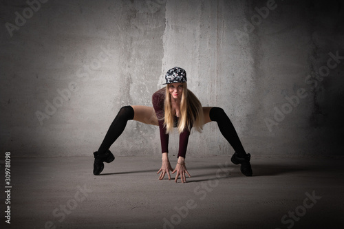Fototapeta Naklejka Na Ścianę i Meble -  Dancer in a dance pose on a gray background. Blonde dancer with long hair in a sexy pose. Feet, dance, modern dance, hip hop, classical dance, stretching, active, fitness body