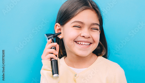Laughing mixed race girl with otoscope. Concept hearing exam