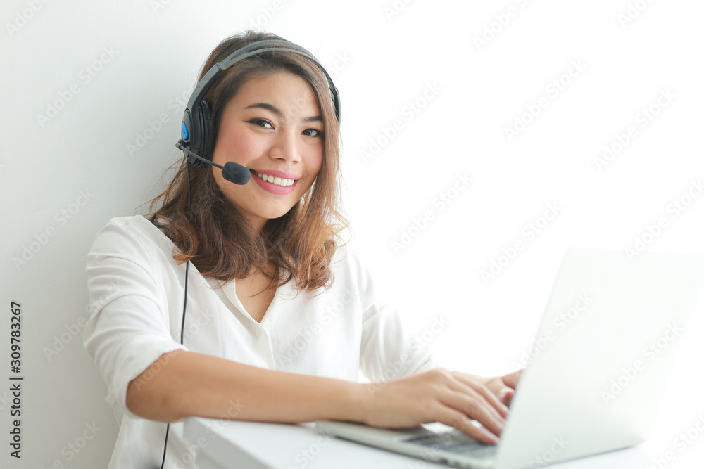 Asian woman on white shirt speak with headphone and using laptop on white background smile and happy face operator concept Asian woman on white shirt speak with headphone and using laptop on white background smile and happy face operator concept