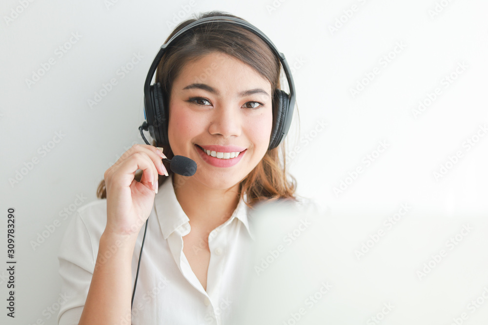 Asian woman on white shirt speak with headphone and using laptop on white background smile and happy face operator concept Asian woman on white shirt speak with headphone and using laptop on white background smile and happy face operator concept