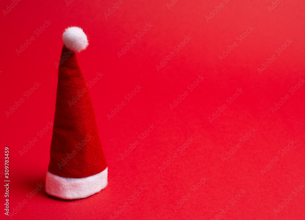 Santa hat on the bright red background as the Christmas concept (minimal style), copy space on the right for your text Santa hat on the bright red background as the Christmas concept (minimal style), copy space on the right for your text