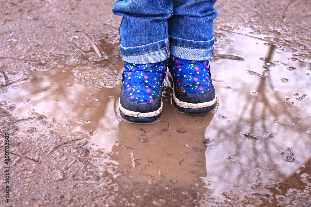 Kids boots in muddy puddle. Colorful winter outdoor rain shoes on childrens feet in action. A