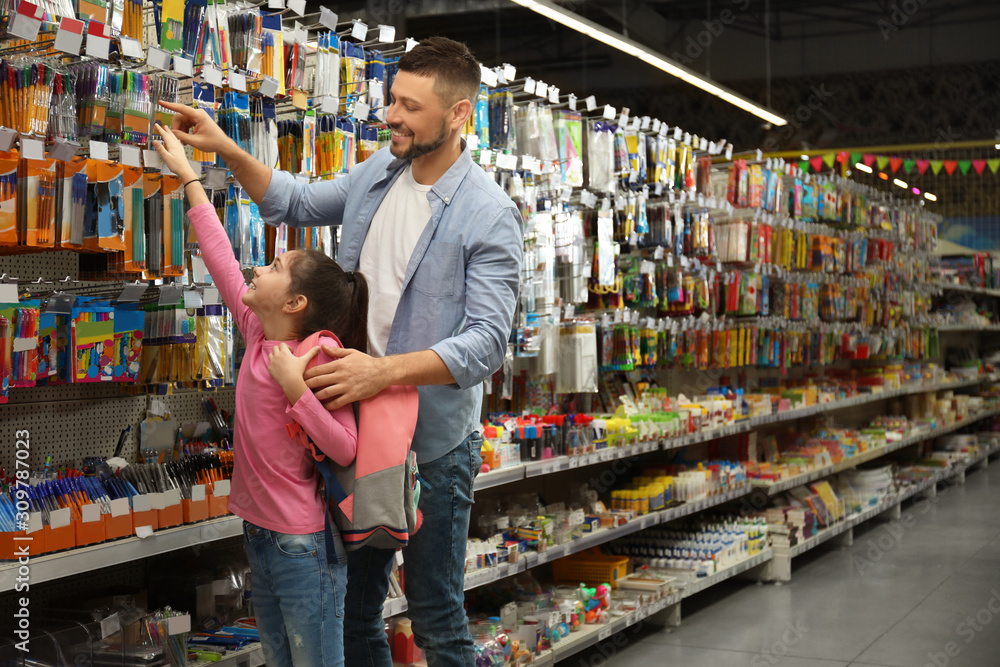 Little girl with father choosing school stationery in supermarket
