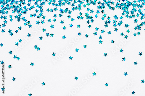 Iridescent Blue color falling stars. Glitter confetti on white festive background. Holiday Sparkling Frame. Flat lay.