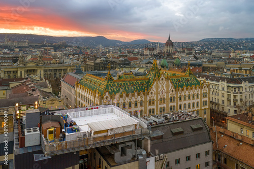 Amazing roof in Budapest.State Treasury building with Hungarian Parliament in winter time.    All tiles on the roof made from the world famous Zsolnay pyro granite. Rootfop ice rink in the foreground. photo