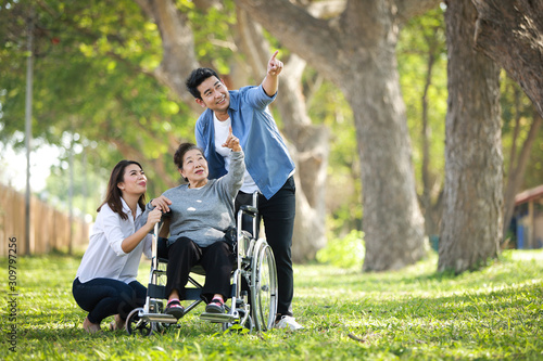 Asian senior woman sitting on the wheelchair with family happy smile face on the green park