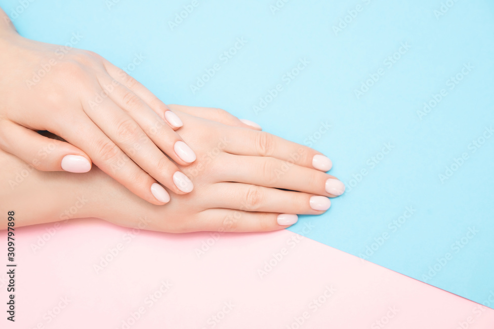 Beautiful female hands with stylish nail manicure gel polish on pink and blue background, top view. Skin care concept