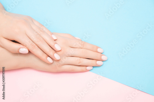 Beautiful female hands with stylish nail manicure gel polish on pink and blue background  top view. Skin care concept