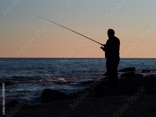 Silhouette of a fisherman. On the background of the sea and sky after the sunset