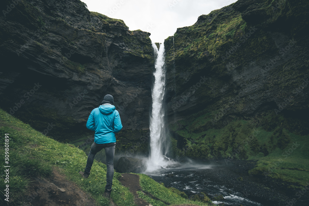 young man standing infront of the Kvernufoss waterfall near skogafoss in southern iceland watching the water flow enjoying his travel young man standing infront of the Kvernufoss waterfall near skogafoss in southern iceland watching the water flow enjoying his travel