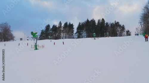Unrecognizable people on ski T-bar lift and schussing from slope in ski resort, handheld. Snow hill, skiers on surface lift and going down a mountain at winter. Climbing and skiing families. Holidays