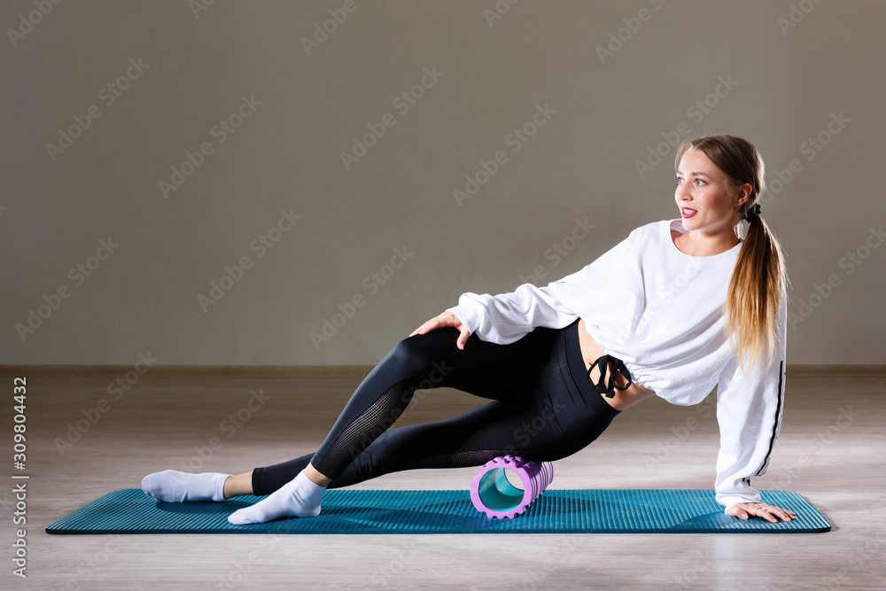 A beautiful slim young girl of European appearance demonstrates exercises with a gymnastic roller for yoga and relaxing her back. A beautiful slim young girl of European appearance demonstrates exercises with a gymnastic roller for yoga and relaxing her back.