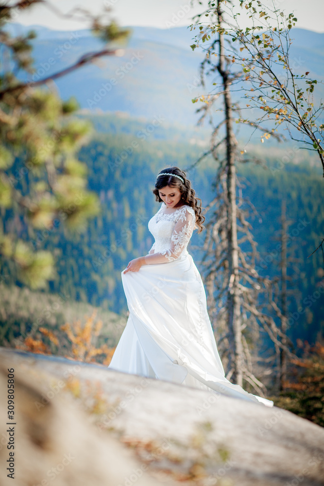 Back of girl in wedding dress sitting on rocks in mountains and looking to fjord, hiking in hills