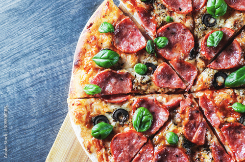 Pepperoni Pizza with Mozzarella cheese, salami, Tomatoes, olive, pepper, Spices and Fresh Basil. Italian pizza on wooden table background