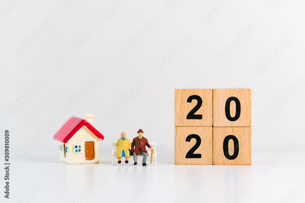 Miniature people, elderly lover sitting with mini house and year 2020 wooden block using as job retirement and family concept