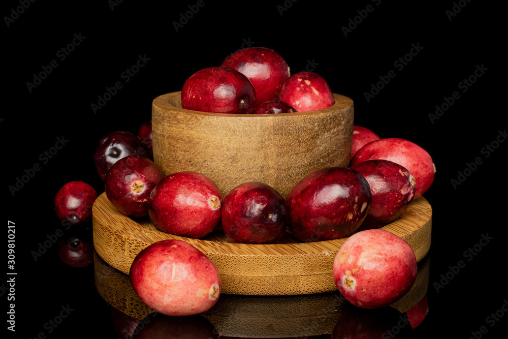 Lot of whole fresh red cranberry in bamboo bowl on round bamboo coaster isolated on black glass Lot of whole fresh red cranberry in bamboo bowl on round bamboo coaster isolated on black glass