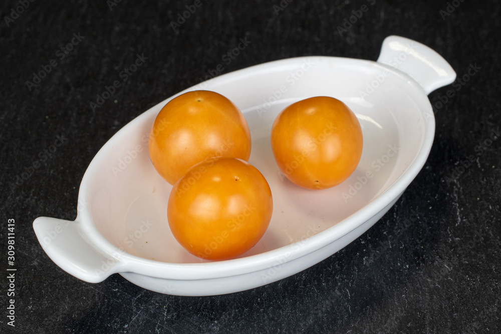 Group of three whole fresh orange physalis on white ceramic plate on grey stone Group of three whole fresh orange physalis on white ceramic plate on grey stone