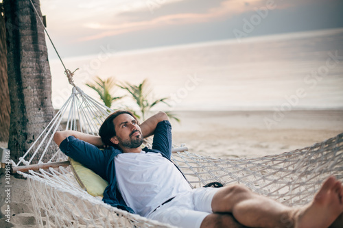 A man enjoys calm, lies in a hammock on the background of the ocean and sunset. © Anna