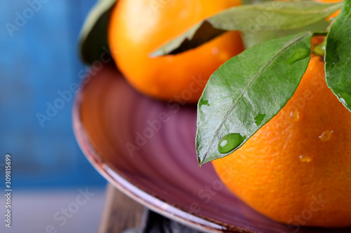 Mandarins with green leaves on the ceramic plate against the blue wooden background