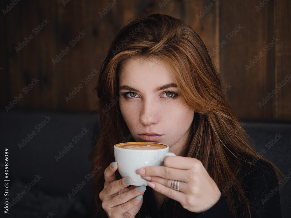 Close up headshot beautiful caucasian red haired woman holding mug drinking cappuccino coffee with latte art adorable smile and feeling good in trendy city cafe Close up headshot beautiful caucasian red haired woman holding mug drinking cappuccino coffee with latte art adorable smile and feeling good in trendy city cafe