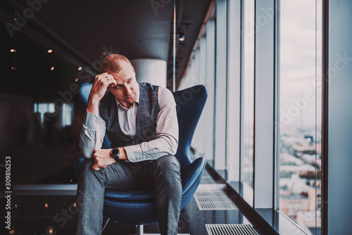 Tableau sur toile An annoyed and depressed caucasian man entrepreneur is sitting on an armchair of
