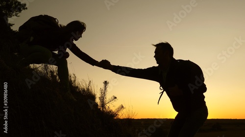 female traveler holds the hand of a male traveler helping to climb top of the hill. Tourists climb mountain at sunset, holding hands. team work of business partners. Happy family on vacation.