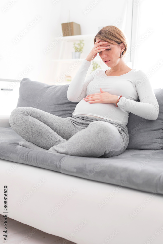 Pregnant tired exhausted woman with stomach and head issues at home on a couch, being sick. Pregnant tired exhausted woman with stomach and head issues at home on a couch, being sick.