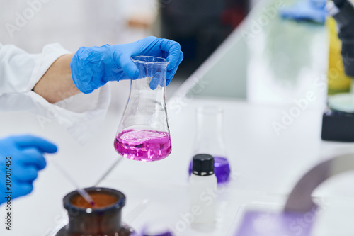 Detail of woman's hands analyzing a sample in an erlenmeyer in the laboratory with potassium permanganate. Real work.